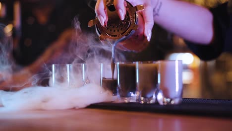 camarero llenando vasos de chupito para fumar con hielo seco con un cóctel colorido