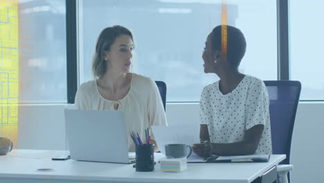 discussing work, two women at office desk with laptops and documents