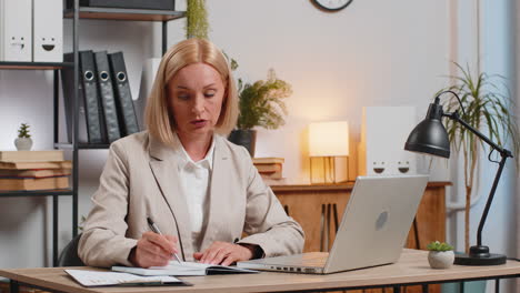 businesswoman writing down or taking down notes while attending online office meeting at home office