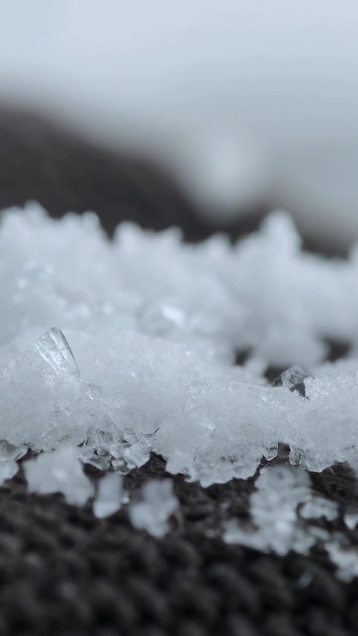 Video verticale: Obiettivo scorrevole che esegue una ripresa macro su un capo a maglia all'aperto, mostrando schegge di ghiaccio e goccioline.
