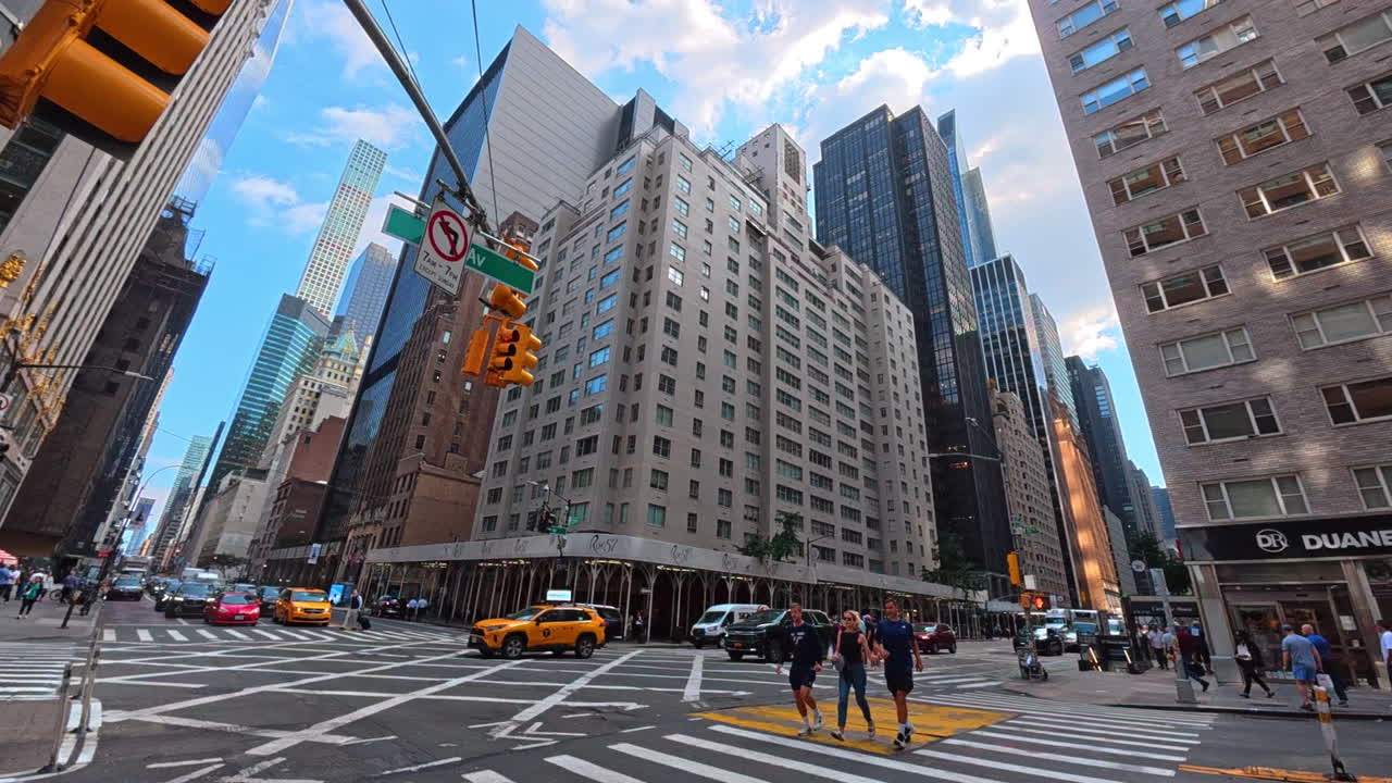 New York, USA, 1 August 2025: Street corner with tall modern buildings in New York City. A busy Manhattan street corner with traffic, skyscrapers, and pedestrians under a bright sky