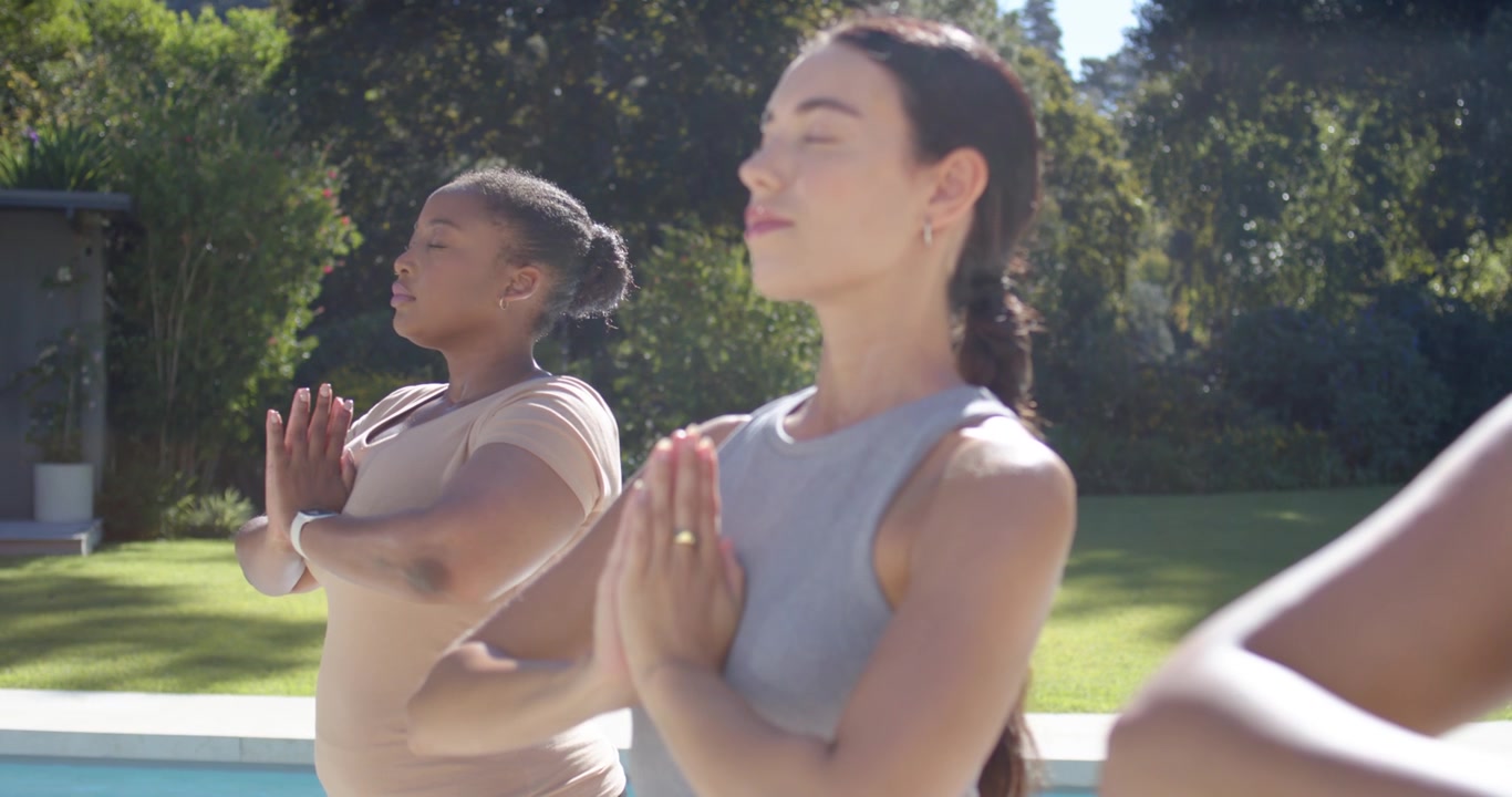 3 iogues mulheres em sincronia, com as mãos em oração, respirando à beira da piscina para calma, expansão e um sorriso centrado.