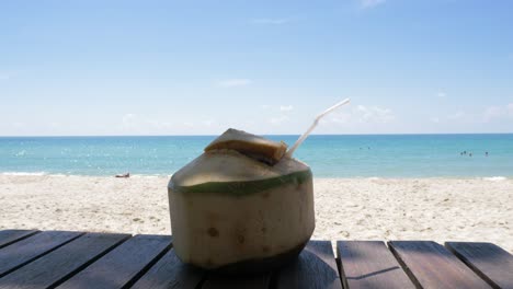 video de una bebida de coco en una mesa de madera en la playa con una vista tranquila y soleada al mar en el horizonte