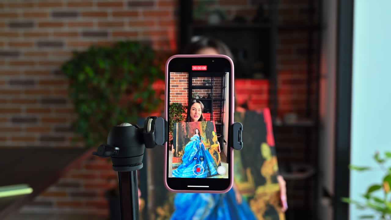 CHISINAU - MOLDOVA, JUNE 06 - 2023: Woman influencer in red dress vlogging on iphone 14 presenting a selfie painting
