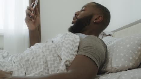 hombre negro conmocionado sentado en la cama. smartphone cayendo de la mano del hombre.
