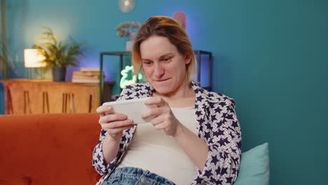mujer jugando con entusiasmo al simulador de carreras o a los videojuegos de disparos en su teléfono inteligente en casa
