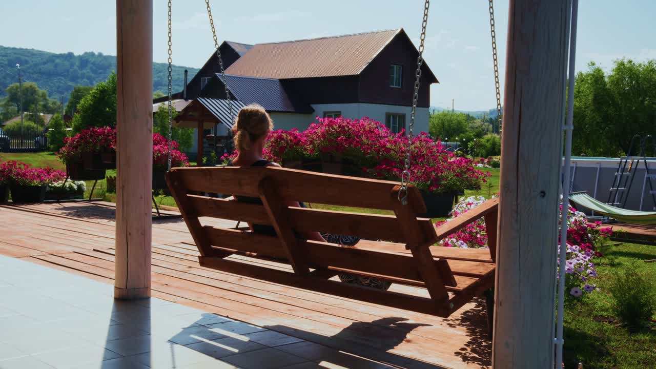 Donna in relax su un'altalena di legno in un giardino soleggiato