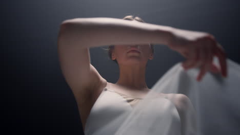 elegant ballerina looking camera indoors. pretty ballet dancer raising hand.