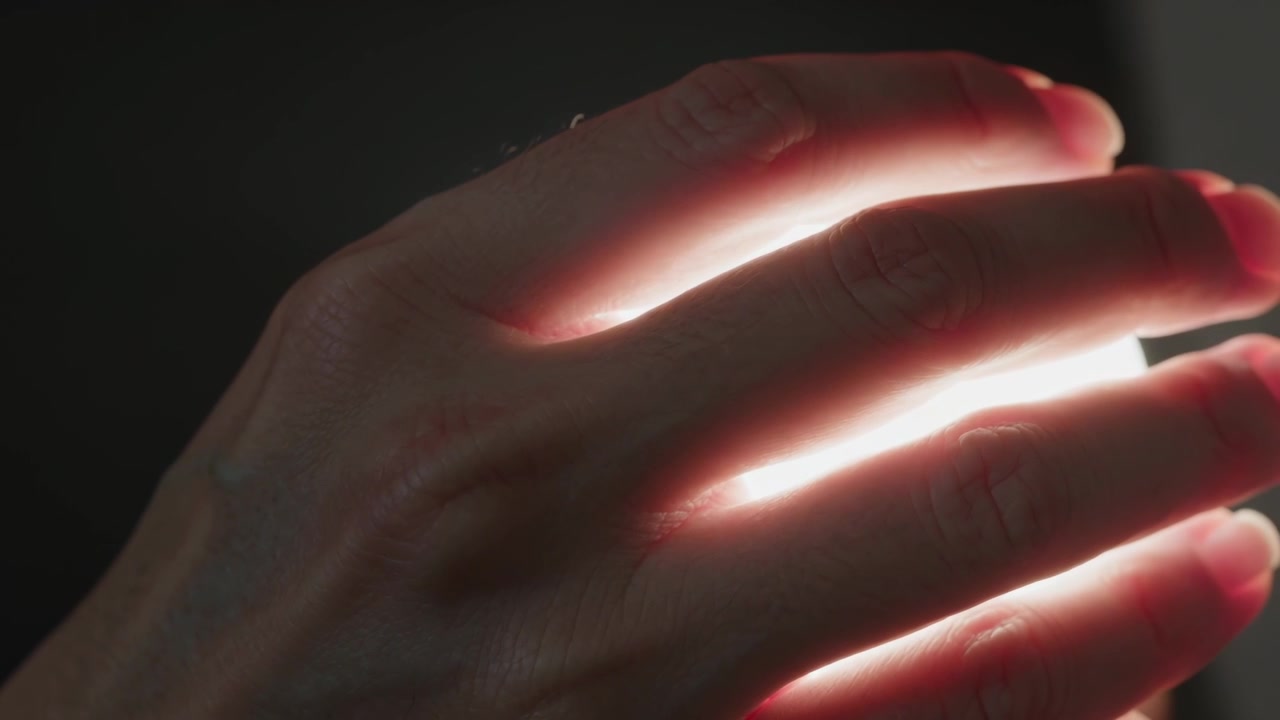 Adjusting adult hand revealing widening backlight between fingers in dim room close-up, lens flare
