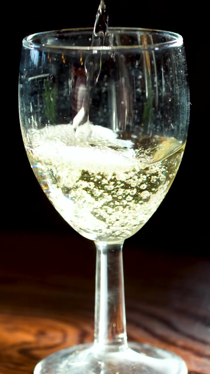 Bevanda frizzante trasparente versata in un bicchiere da vino, tavolo di legno, illuminazione drammatica, primo piano, telecamera fissa