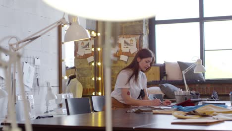 beautiful female fashion designer sitting at desk and drawing sketch of new dress in modern sewing studio 1