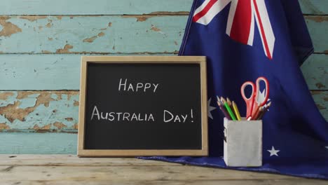 Texto-Del-Feliz-Día-De-Australia-Y-Bandera-Australiana-Con-Estrellas-Y-Artículos-Escolares-En-Una-Mesa-De-Madera