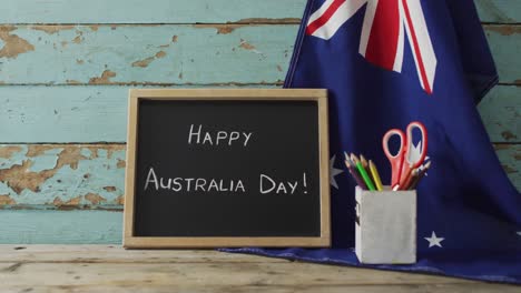happy australia day text and australian flag with stars and school items on wooden table
