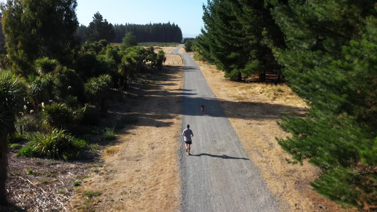 Following man going for a run with his dog on a dirt track in the woods.