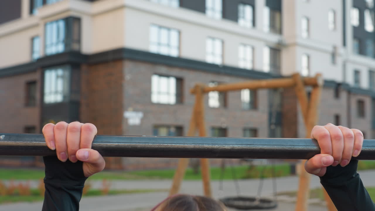 Hand view of energetic trainer exhaling while gripping horizontal pull up bar in urban park gym with autumn foliage backdrop showcasing forearm strength focus and control during calisthenics