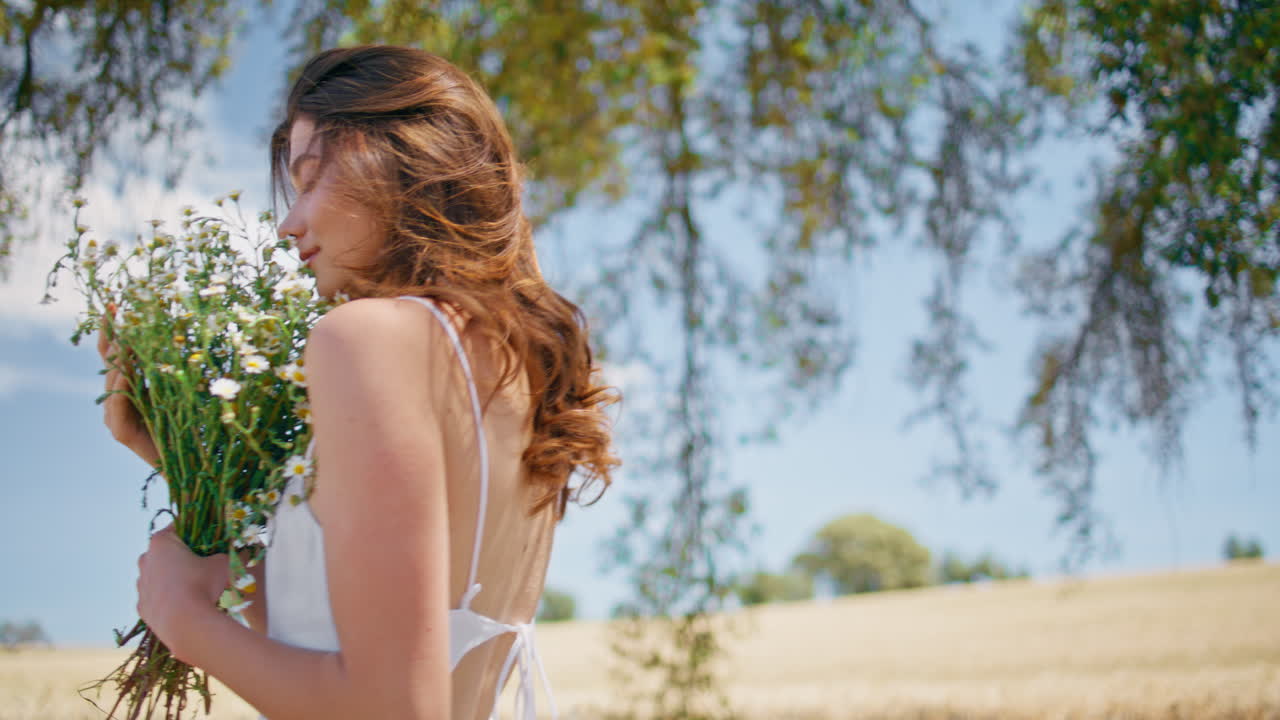Young lady inhaling daisies fragrance summer countryside closeup. Woman walking