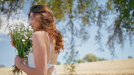 young lady inhaling daisies fragrance summer countryside closeup. woman walking