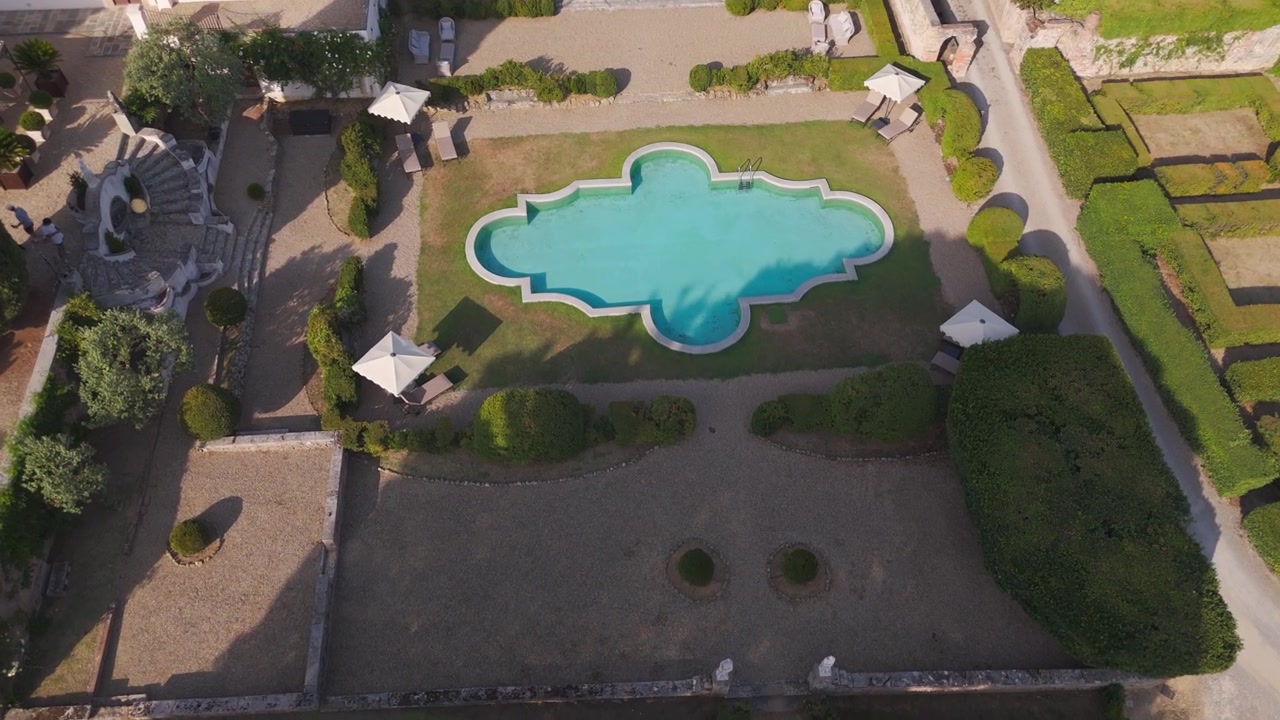 Aerial view descends over ornate pool and manicured gardens at historic villa estate