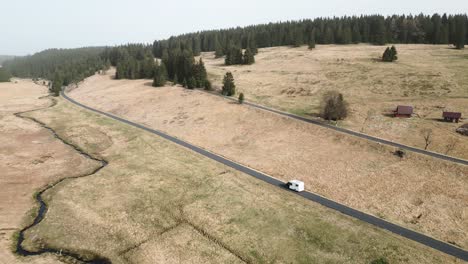 An-aerial-shot-of-a-camper-driving-along-a-winding-road-in-the-middle-of-mountain-moors