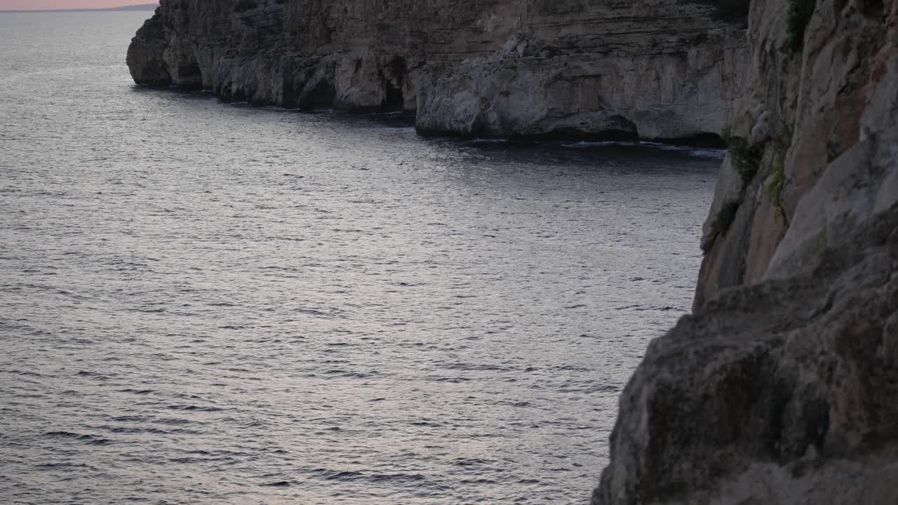 Rocky coastal cliffs meeting the calm Mediterranean waters at Cova D'En Xoroi, Menorca