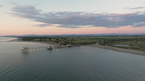 vista aérea en cámara lenta de cabañas de pesca a orillas del estuario al atardecer, máquina de pesca italiana, llamada "trabucco" ravenna cerca del valle de comacchio