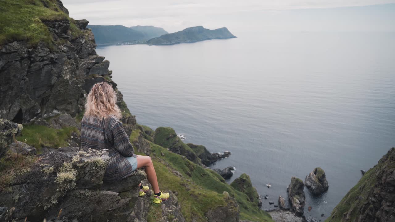 mujer rubia con zapatillas amarillas sentada en lands end en runde island, noruega