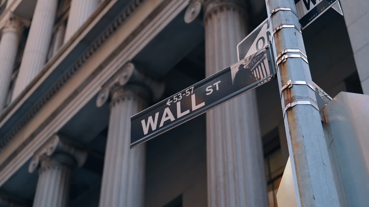 Vejskilt med inskriptionen Wall Street. Lav vinkel. Grå bygning med søjler i baggrunden. New York, USA