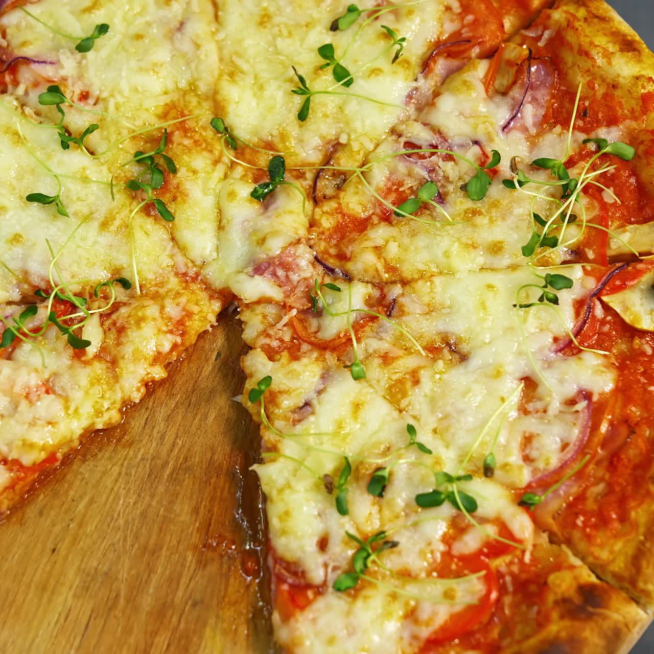 Fresh pizza spinning on the table. Delicious pastry with melted cheese, tomatoes and meat in pizzeria. Well baked pizza without one portion on table