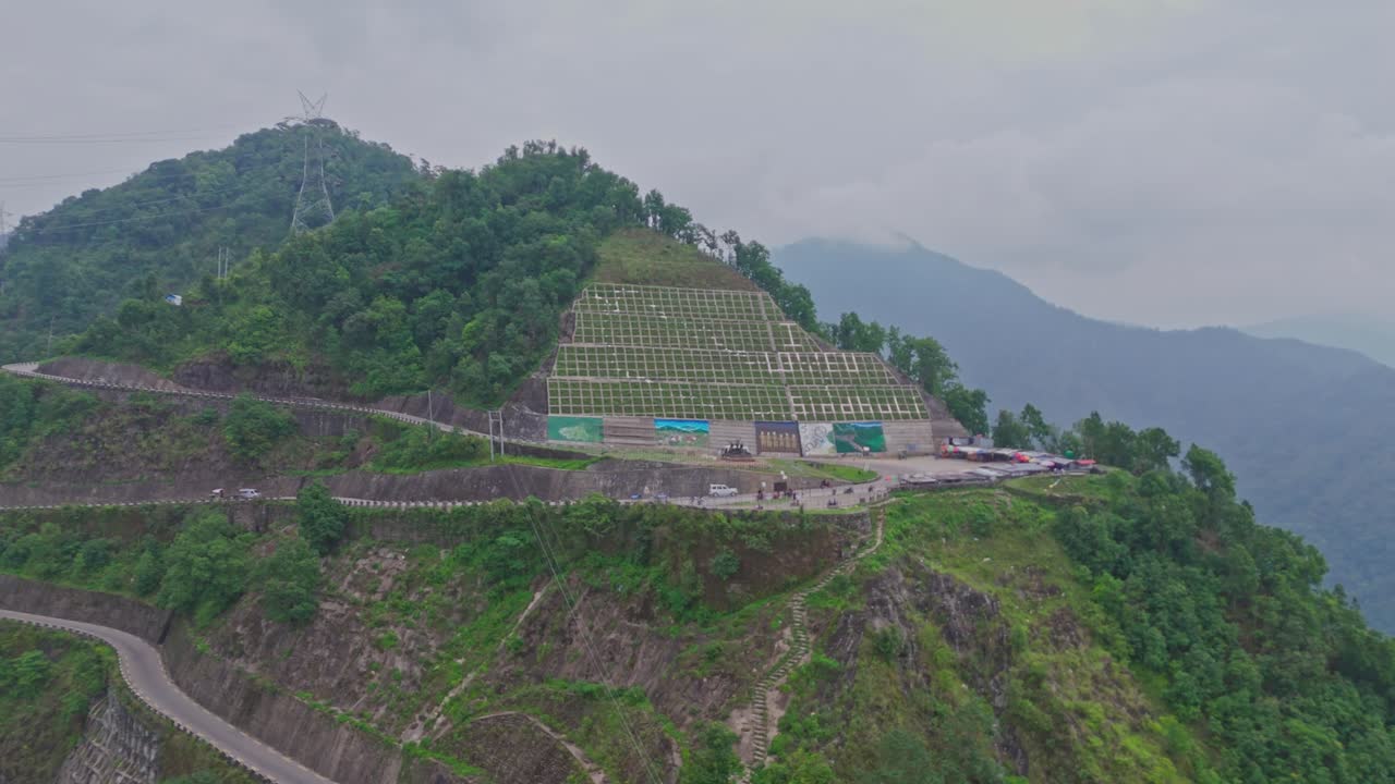 A serpentine road curves gracefully through vibrant green mountains, offering a breathtaking view of natural beauty and human engineering in harmony, captured from a high-altitude aerial perspective.