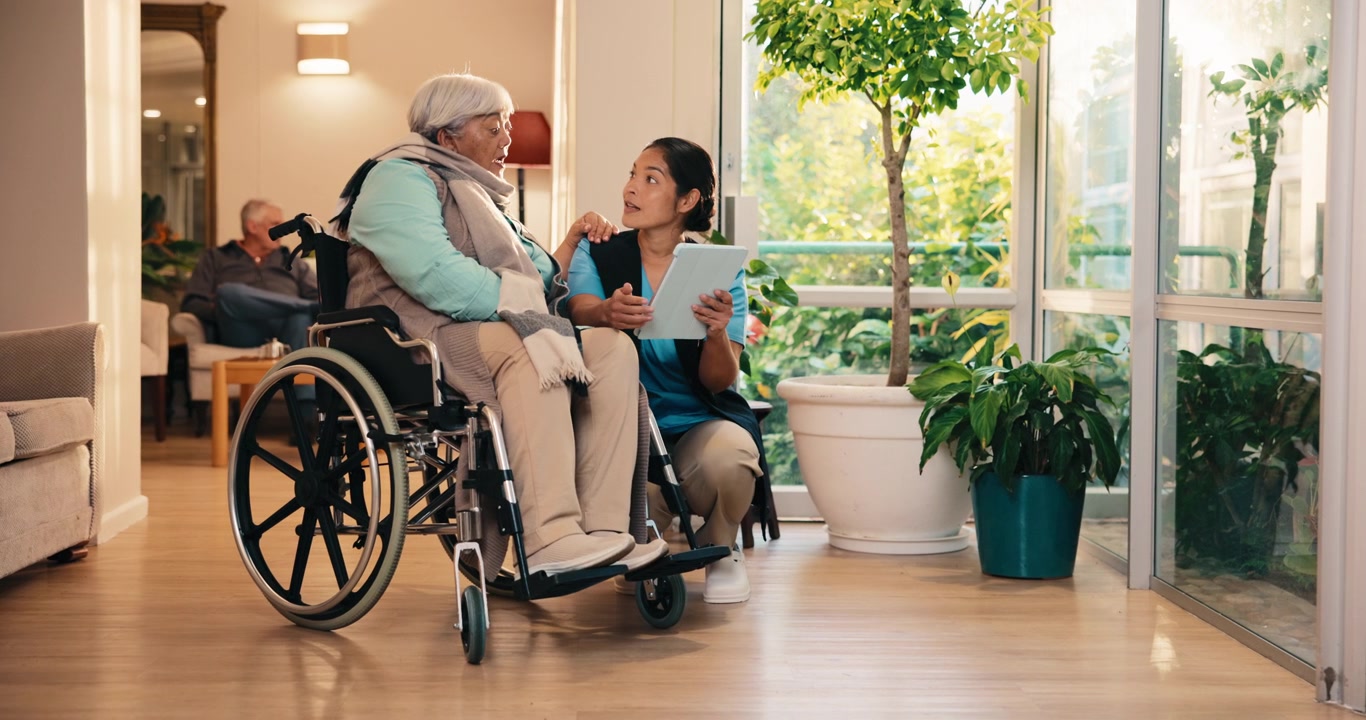 Caregiver che mostra un tablet a un'anziana su una sedia a rotelle