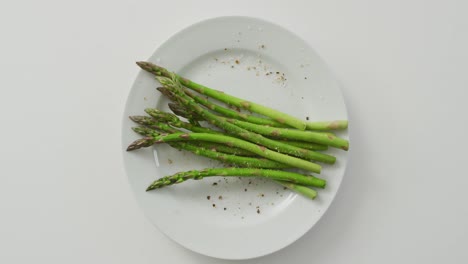 Video-of-fresh-asparagus-stalks-on-white-plate-over-white-background