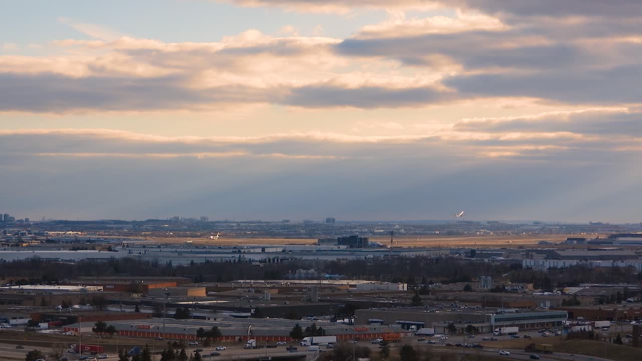 Wide static view of the Toronto airport on a partly cloudy day in the middle of winter with rays of sun coming down and traffic along the freeway