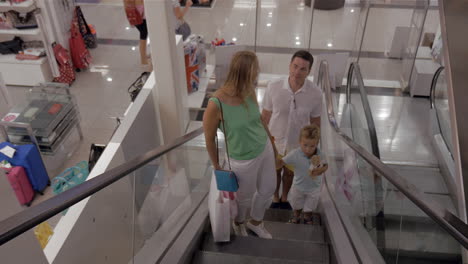 young family with child riding escalator in shopping center