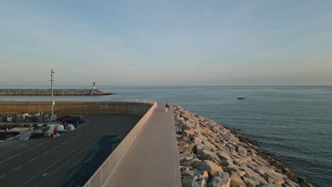 Menschen-Gehen-Auf-Dem-Bürgersteig,-Strandküste-Von-Arenys-De-Mar,-Katalonien,-Spanien,-Drohnenaufnahme-Der-Skyline-Am-Meer