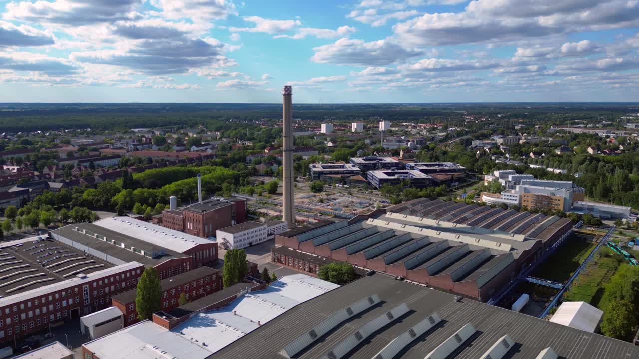 industrial buildings and a chimney in Hennigsdorf, Germany, with a train passing by. Unique aerial view flight fly reverse drone