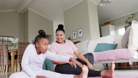 Happy-unaltered-african-american-mother-and-daughter-doing-yoga-stretching-at-home,-in-slow-motion