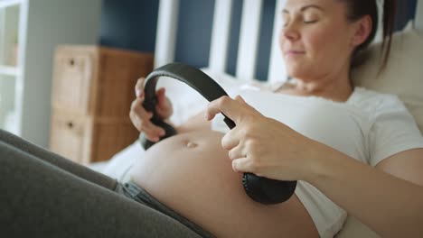 tracking video of pregnant woman putting headphones on pregnant abdomen.