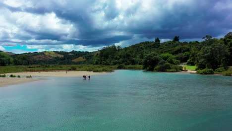 gente cruzando un río azul poco profundo en un día nublado en nueva zelanda