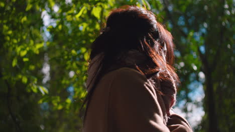 Close-up-low-angle-of-woman-with-coat-and-scarf-under-trees-in-sunny-day