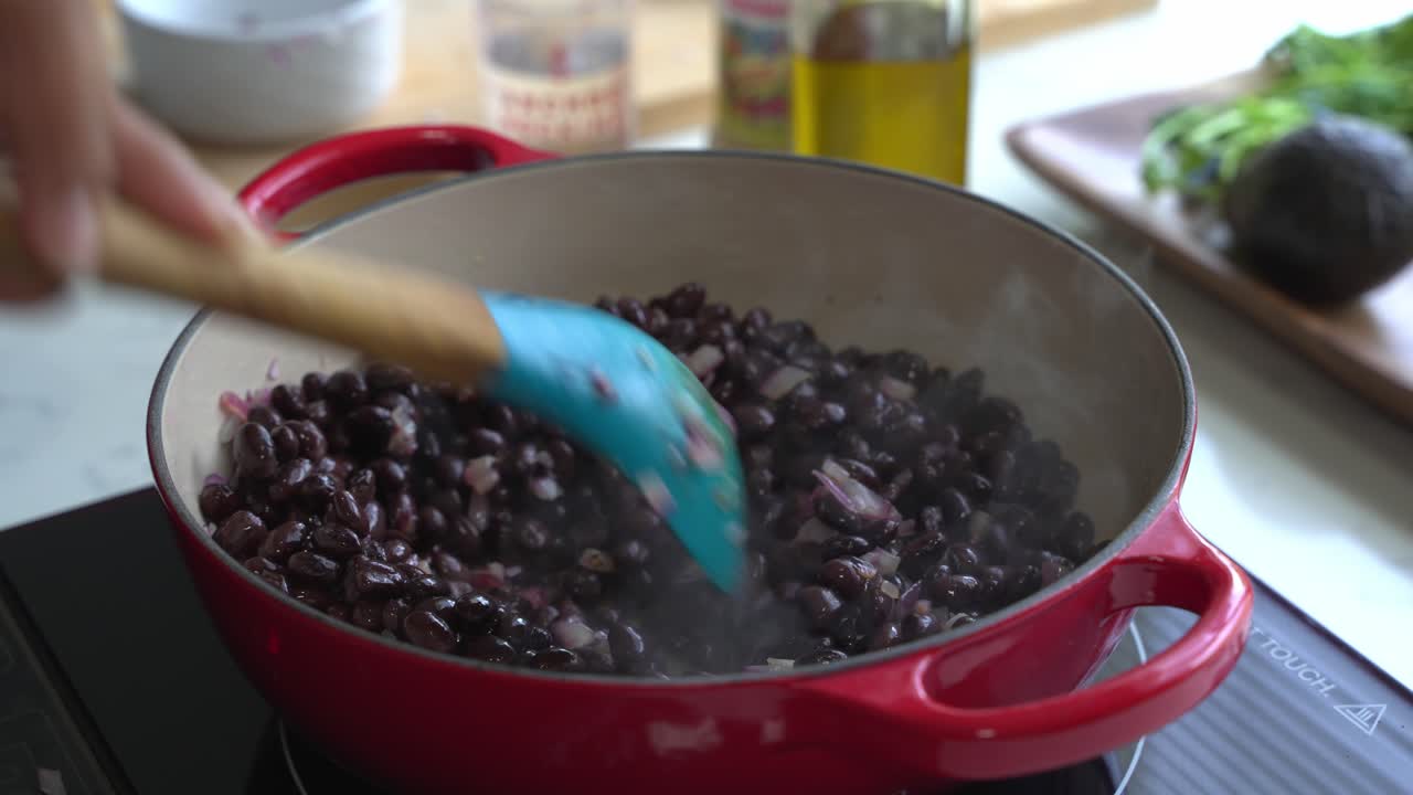cocinar frijoles negros dentro de una olla de hierro fundido cocinar una comida dos latas de frijoles arroz plátano aguacate cebolla roja y cilantro