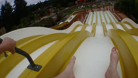 launching down a waterslide in public bath or water park, slow motion, landing in a splash of water next to a young man, not recognizable