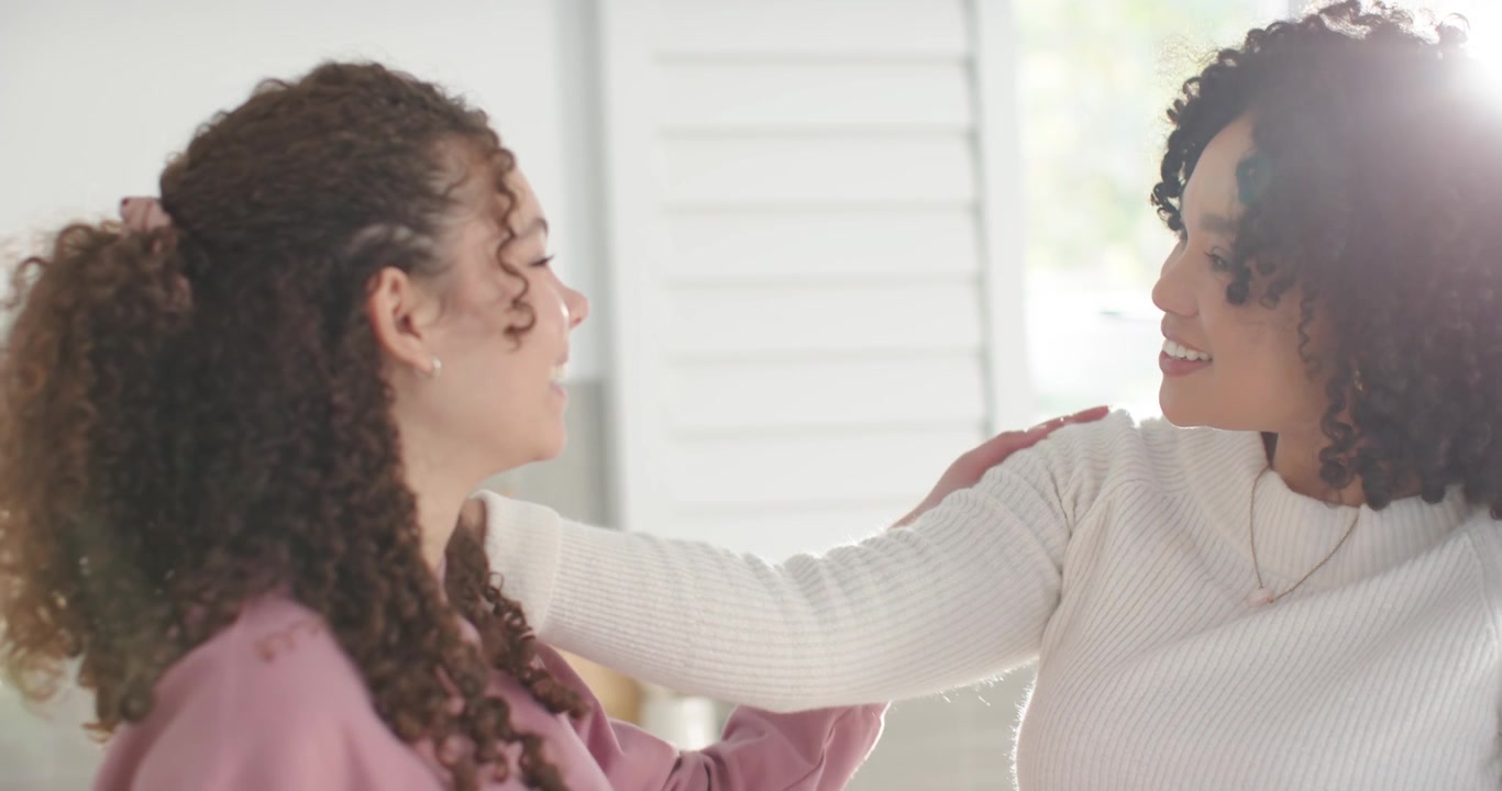 Mamma afroamericana che conforta la figlia adolescente dopo essersi scambiate sorrisi, toccandosi la spalla in cucina.