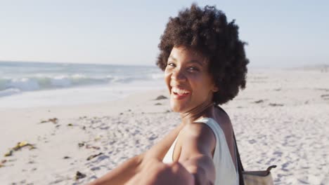 Portrait-of-smiling-african-american-woman-holding-hand-on-sunny-beach