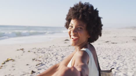retrato de una mujer afroamericana sonriente de la mano en una playa soleada