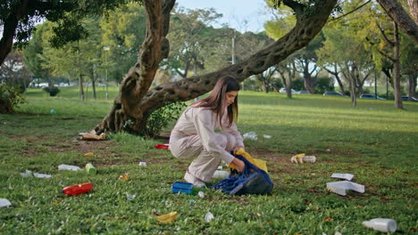 una niña limpia la contaminación del parque recogiendo desechos orgánicos de plástico de la hierba verde.