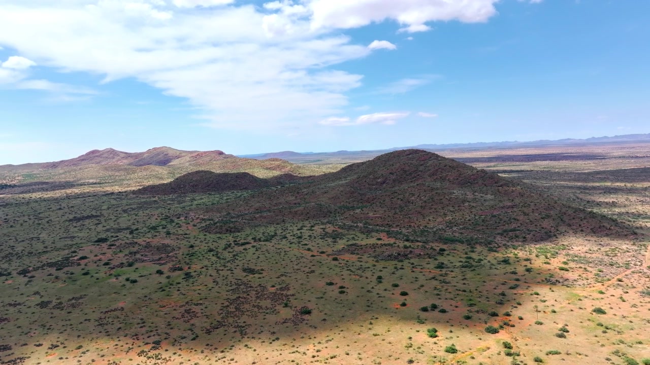 Vista drone di una solitaria collina desertica circondata da vaste pianure aride e bassa macchia. Brulle colline rocciose e macchia secca si estendono fino all'orizzonte attraverso questo remoto terreno bruciato dal sole