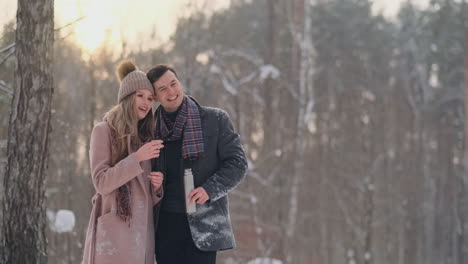 A-loving-couple-man-and-woman-in-the-winter-forest-drinking-tea-from-a-thermos.-Stylish-man-and-woman-in-a-coat-in-the-Park-in-winter-for-a-walk.-Slow-motion