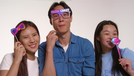 Group-Of-Young-Friends-In-Front-Of-White-Studio-Background-Having-Fun-Posing-For-Photo-Booth-Style-Portraits-With-Props