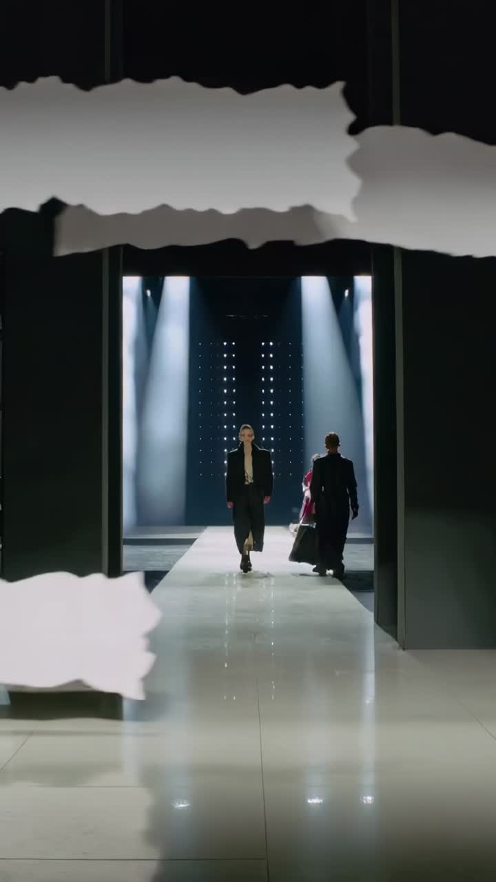 Vertikal video: Gående model skrider frem på catwalk, overlay afslører frakke og taske til show.