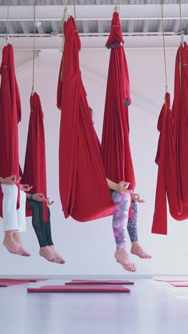 relaxed women hold fingers in gyan mudra position meditating and sitting in fly yoga hammocks in white room